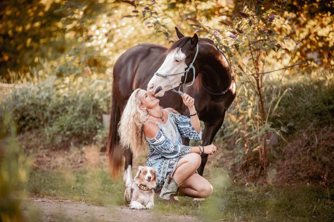 Caro kniet mit ihrem Schecken und dem Hund im Herbstlaub