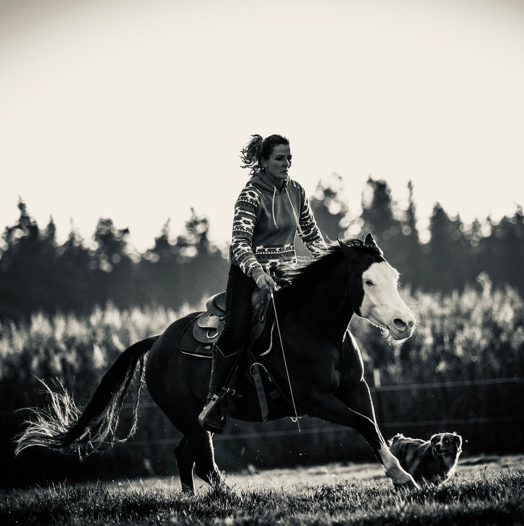 Schwarz-Weiß-Foto: Caro reitet Freddie frei im Galopp, der Hund läuft mit