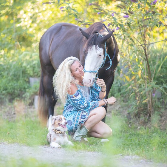 Caro sitzt mit Pferd und Hund im Gras